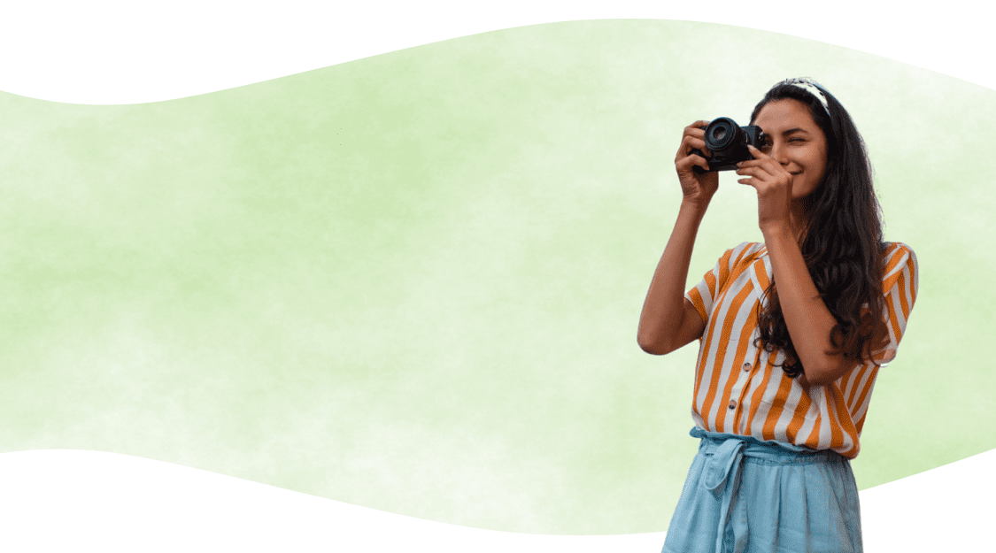 Smiling woman using a camera, perfecting her skills with photography cheat cards, against a light green background.