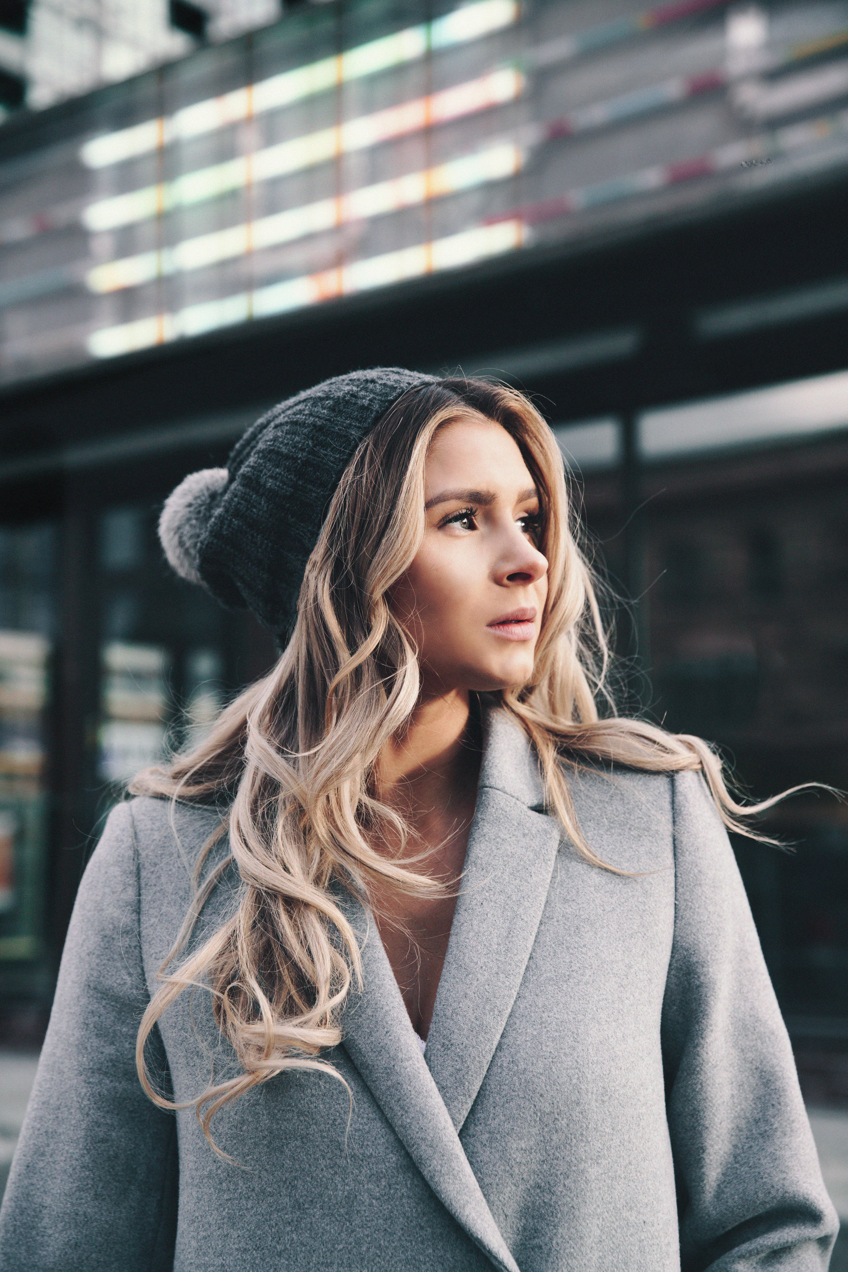 Businesswoman wearing a wool hat, looking thoughtful in an outdoor urban setting.