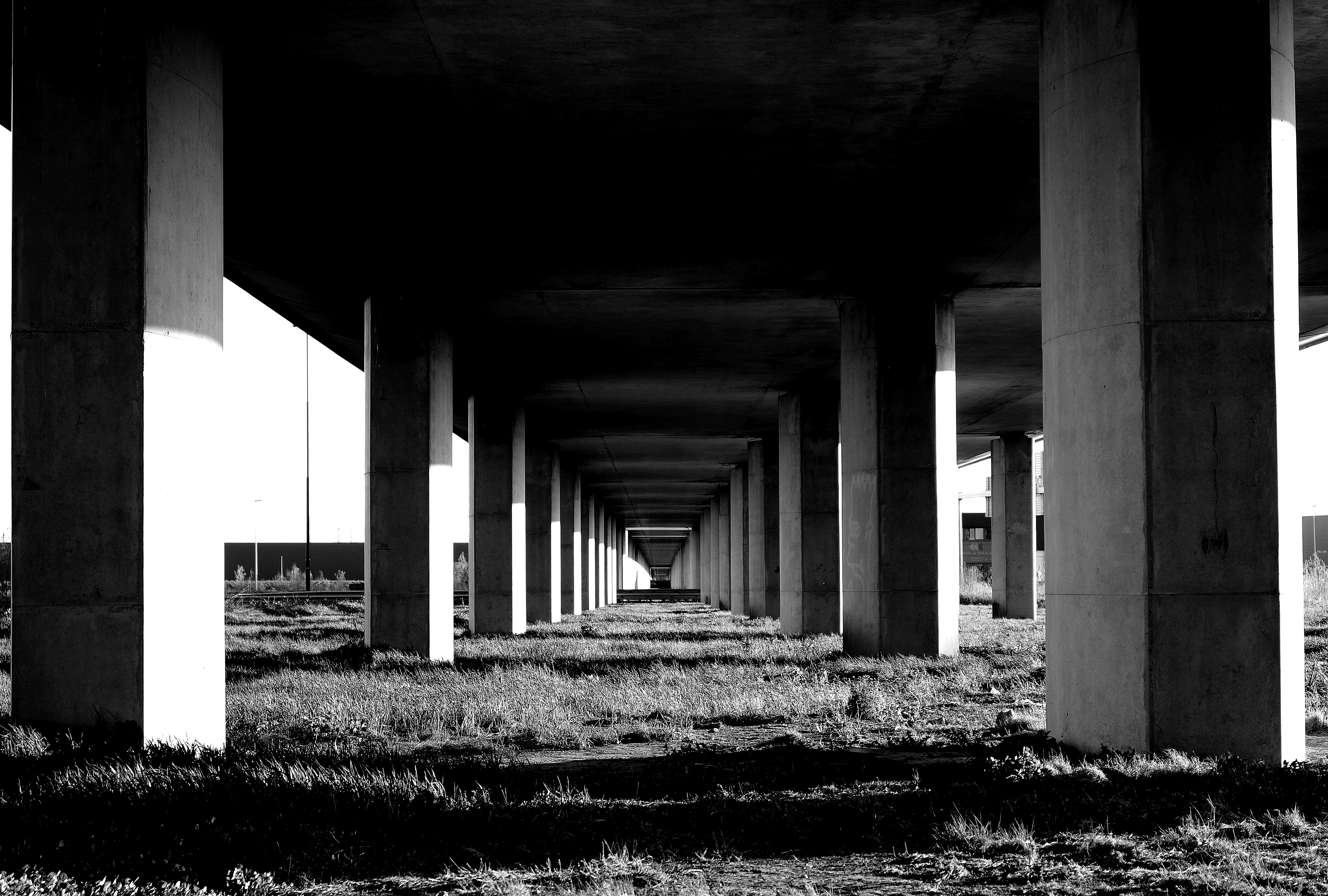 Black and white image of a long corridor with repeating arches and dramatic light and shadow patterns, creating a sense of depth and symmetry.