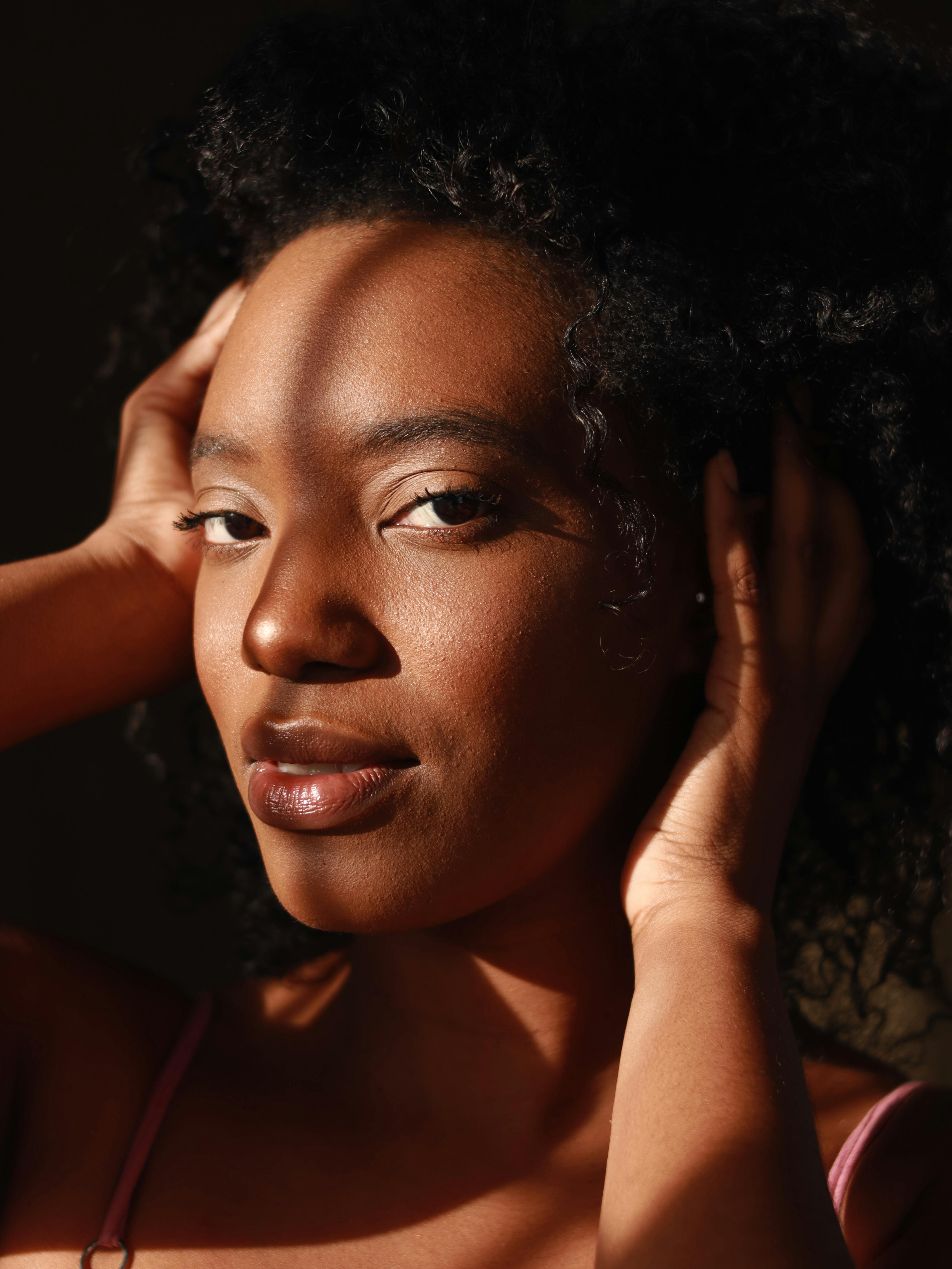 Portrait of a woman with curly hair in soft natural light, casting shadows across her face, with a calm and confident expression.